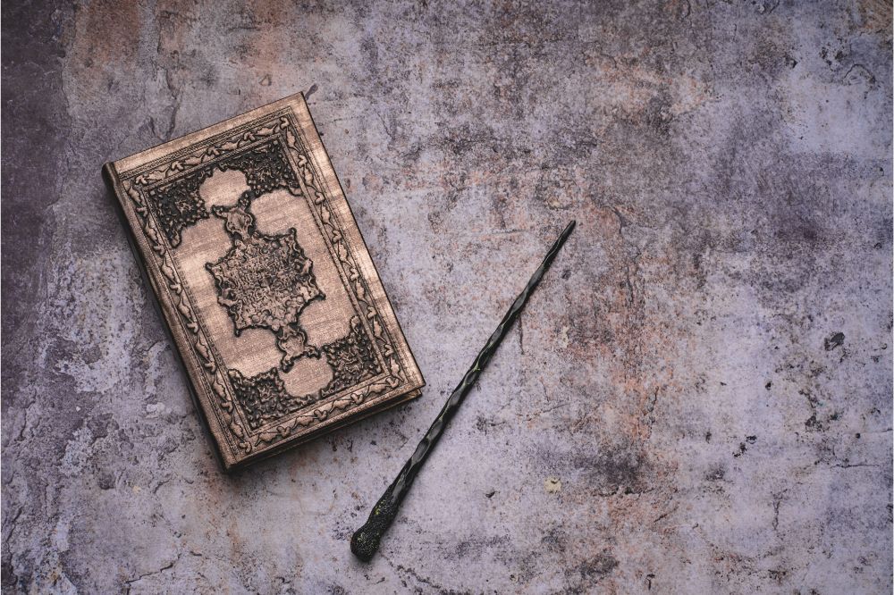 Old book with spells and magic wand on gray background